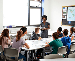 female-high-school-tutor-standing-by-table-with-st-2024-